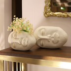 Two decorative face-shaped vases on a wooden table with a mirror in the background.