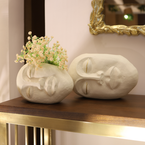 Two decorative face-shaped vases on a wooden table with a mirror in the background.