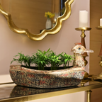 Decorative pot with plants on a table next to a gold mirror and candle holder.