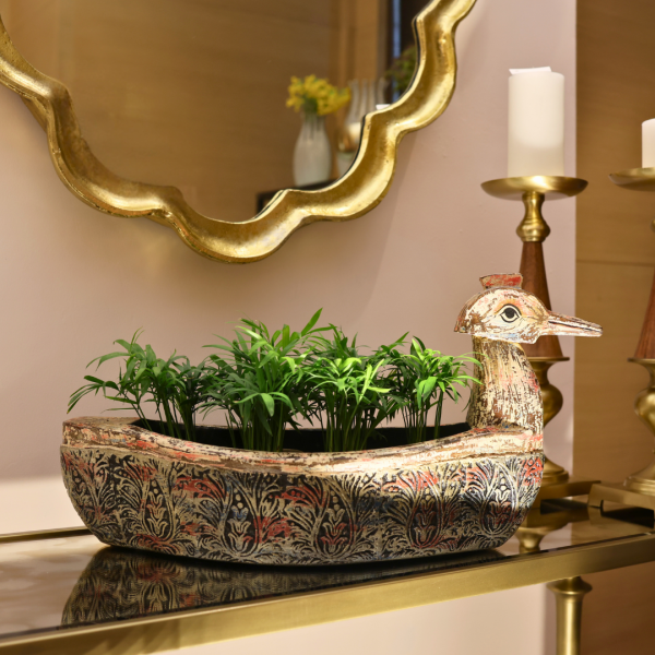 Decorative pot with plants on a table next to a gold mirror and candle holder.