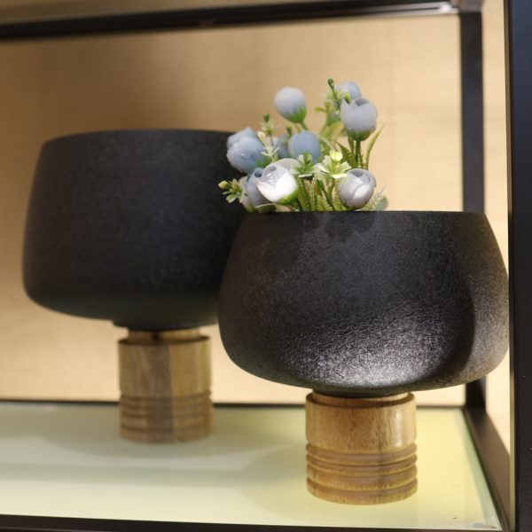 Two black ceramic planters with gold bases on a reflective surface.
