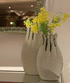 Three textured vases with yellow flowers on a reflective surface.