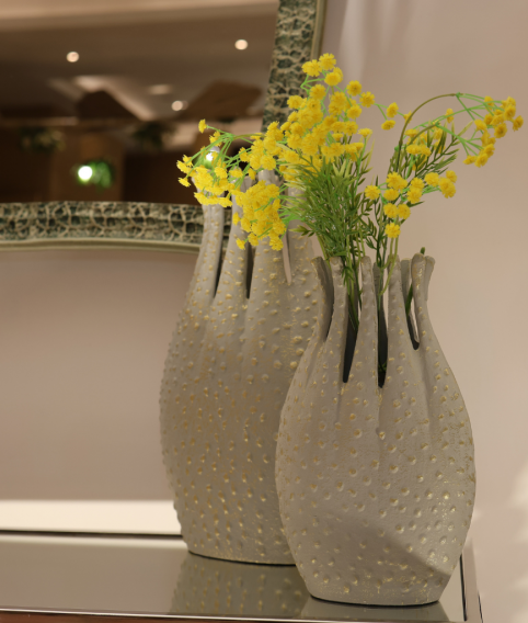 Three textured vases with yellow flowers on a reflective surface.