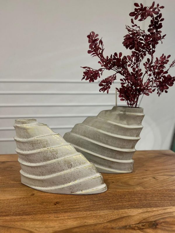 Two aluminium vases with wavy design on a wooden surface, one with dried red flowers.