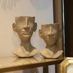 Two stone sculptures of human heads on a shelf with a decorative background