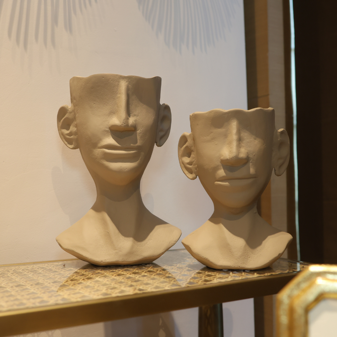 Two stone sculptures of human heads on a shelf with a decorative background