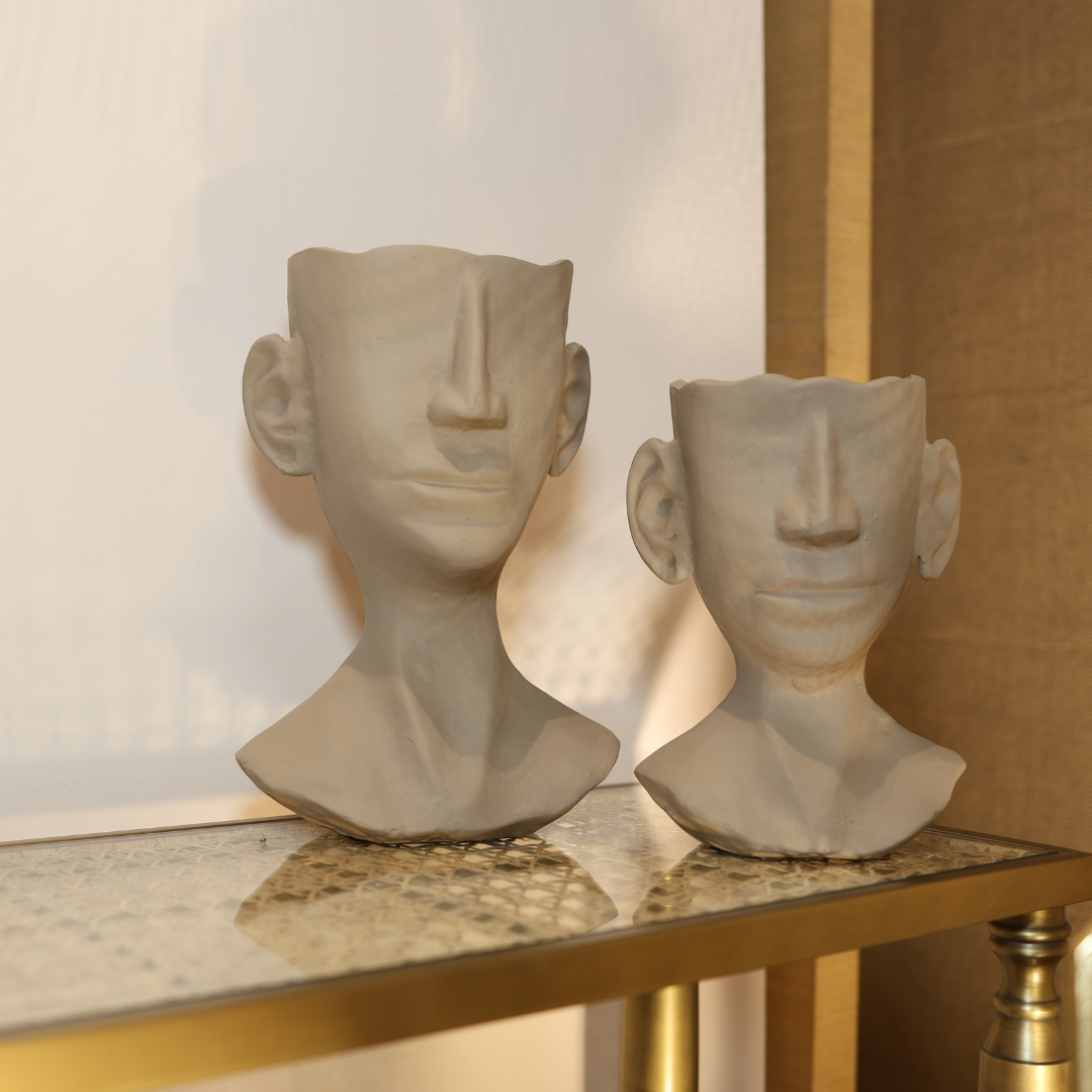 Two ceramic busts on a reflective surface with a blurred background