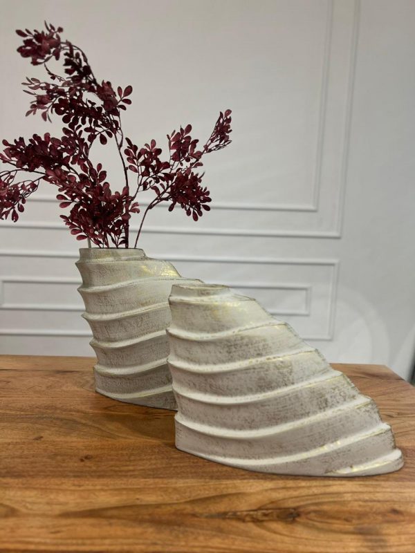 Two wavy-patterned vases with dried red flowers on a wooden surface.