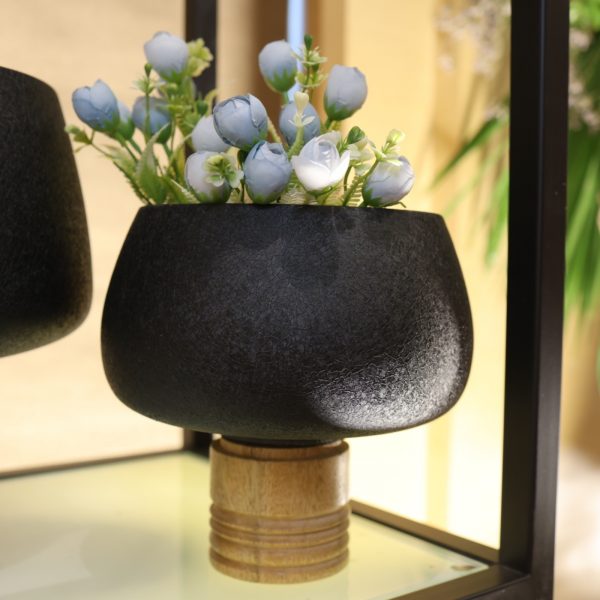 Black steel planter with wooden base and artificial flowers on a reflective surface